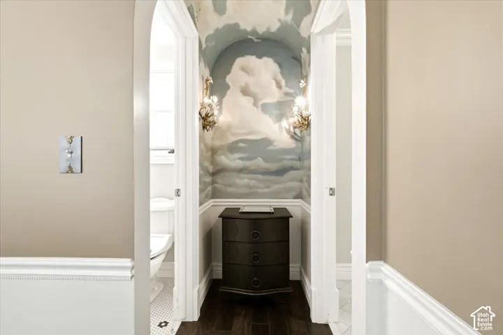 Arched entryway featuring custom wall mural, dark wood-finish flooring, and decorative wall sconces