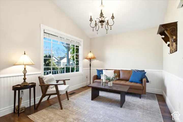 Vaulted ceiling with an ornate chandelier, large window with grid pattern, wood-finish flooring, and wainscoting paneling