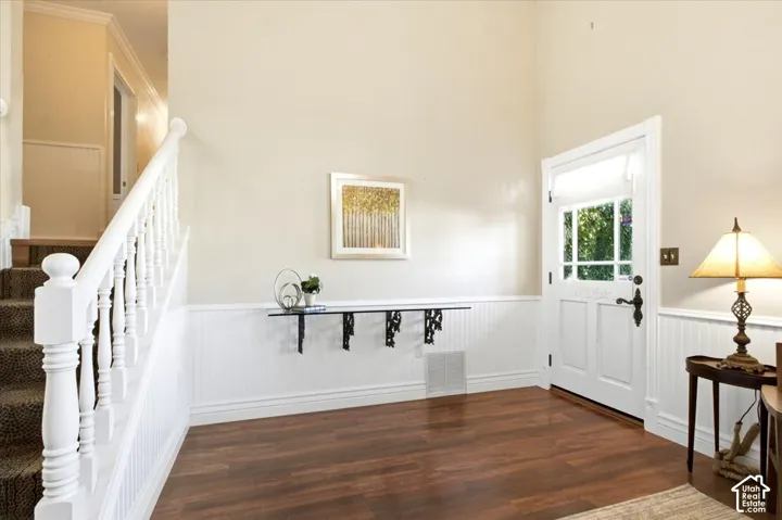 Wood-finish flooring, white wainscoting, a staircase with white balusters, and a glass-paneled entry door