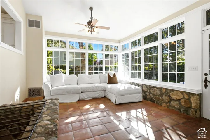 Vaulted ceiling with ceiling fan, extensive grid-pattern windows, stone base wall, terracotta tile flooring, and an integrated stone-clad hearth