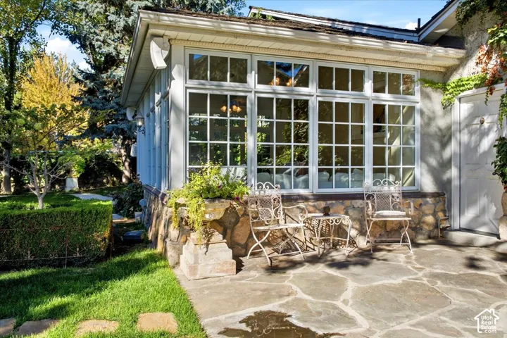 Stone patio featuring an expansive window wall, stone foundation, and a lush green lawn