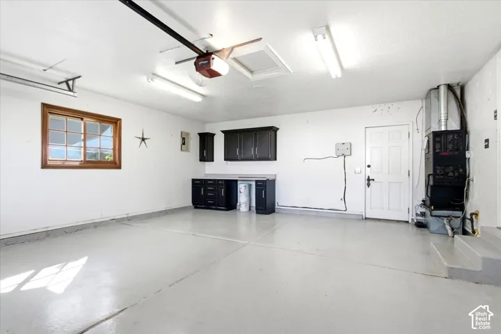 Attached garage featuring a light-colored epoxy floor, built-in cabinetry, a single window with wood-frame trim, and fluorescent lighting fixtures