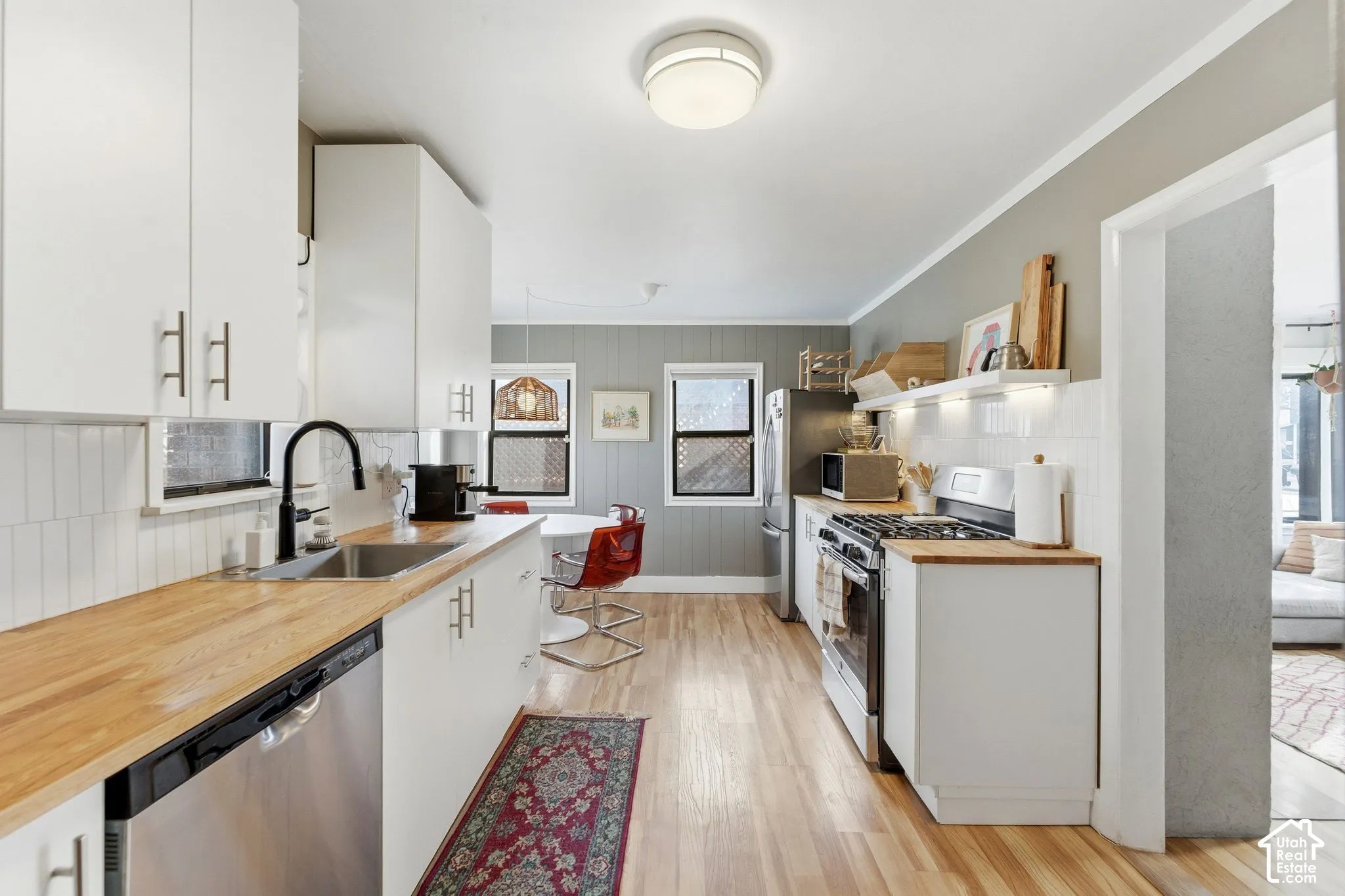 Modern kitchen with wood-finish flooring, white cabinetry, wood-finish countertops, stainless steel appliances, and a white tile backsplash