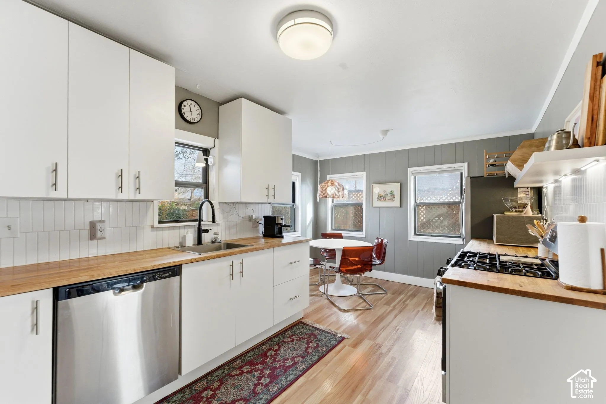 White cabinetry with modern hardware, wood-finish countertops, stainless steel dishwasher, tile backsplash, and a gas range
