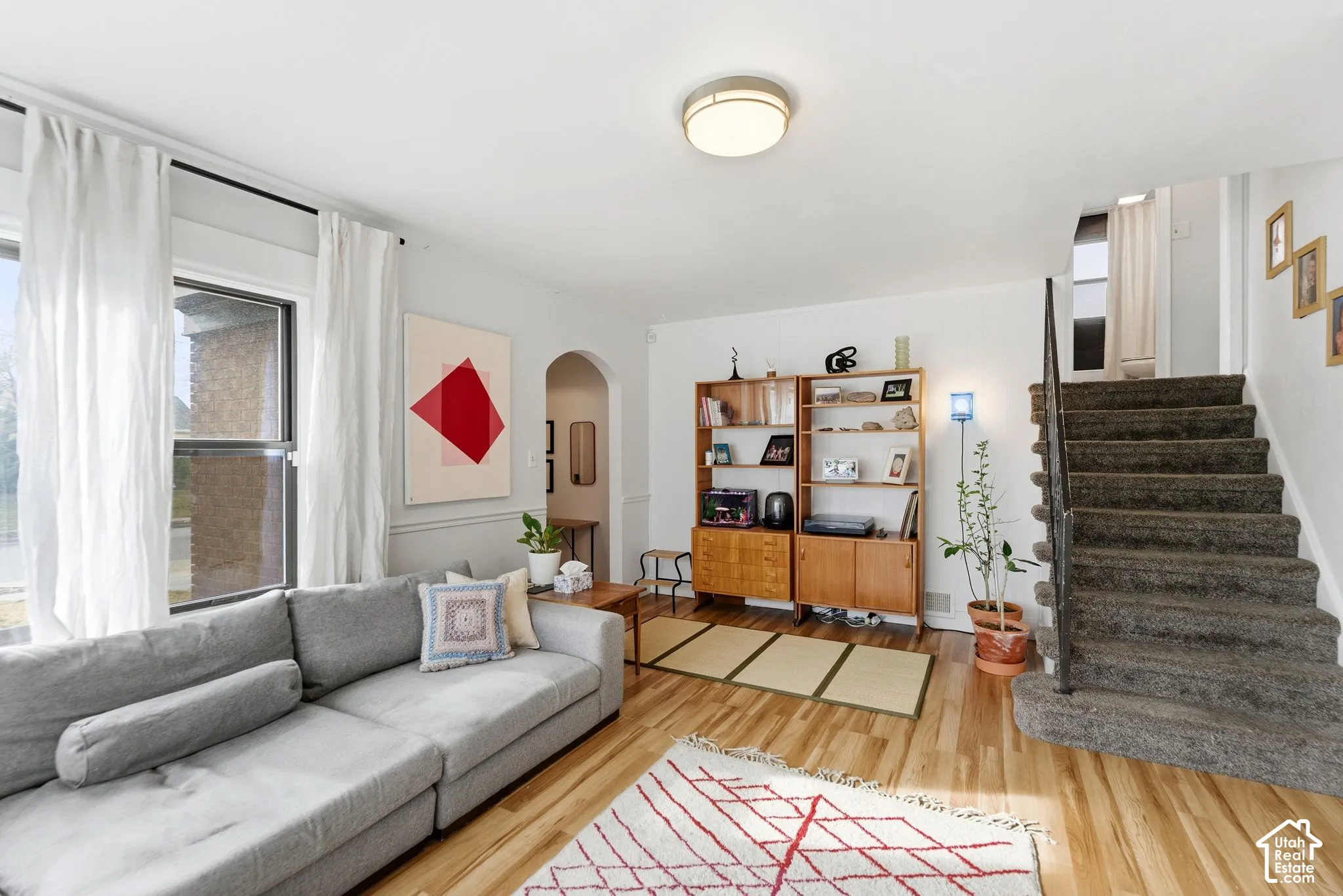 Hardwood flooring, arched doorway, built-in shelving, carpeted staircase with dark railing, and a flush mount ceiling fixture