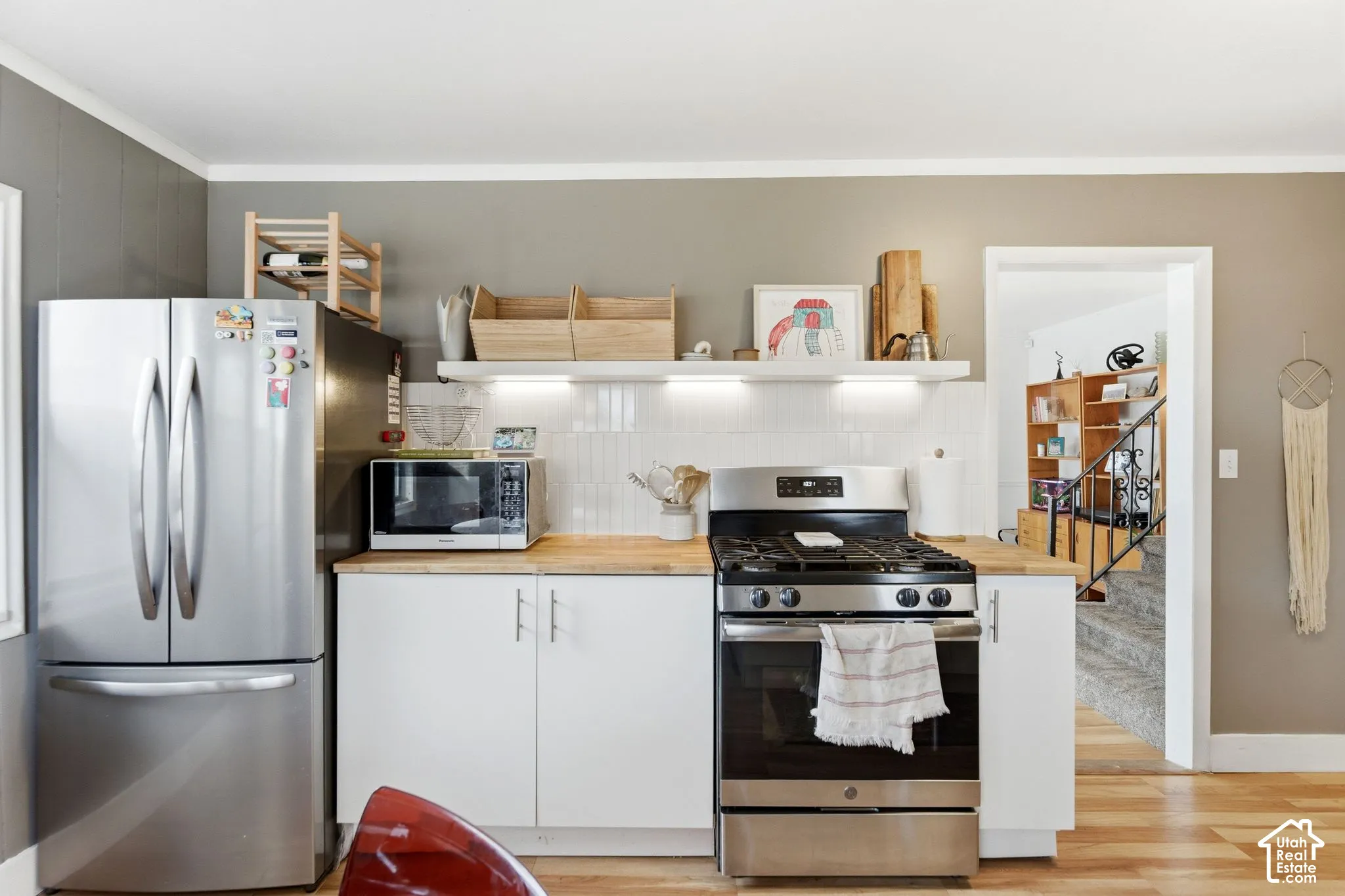 Stainless steel appliances, wood-finish flooring, white cabinetry, light wood countertops, and a white tile backsplash