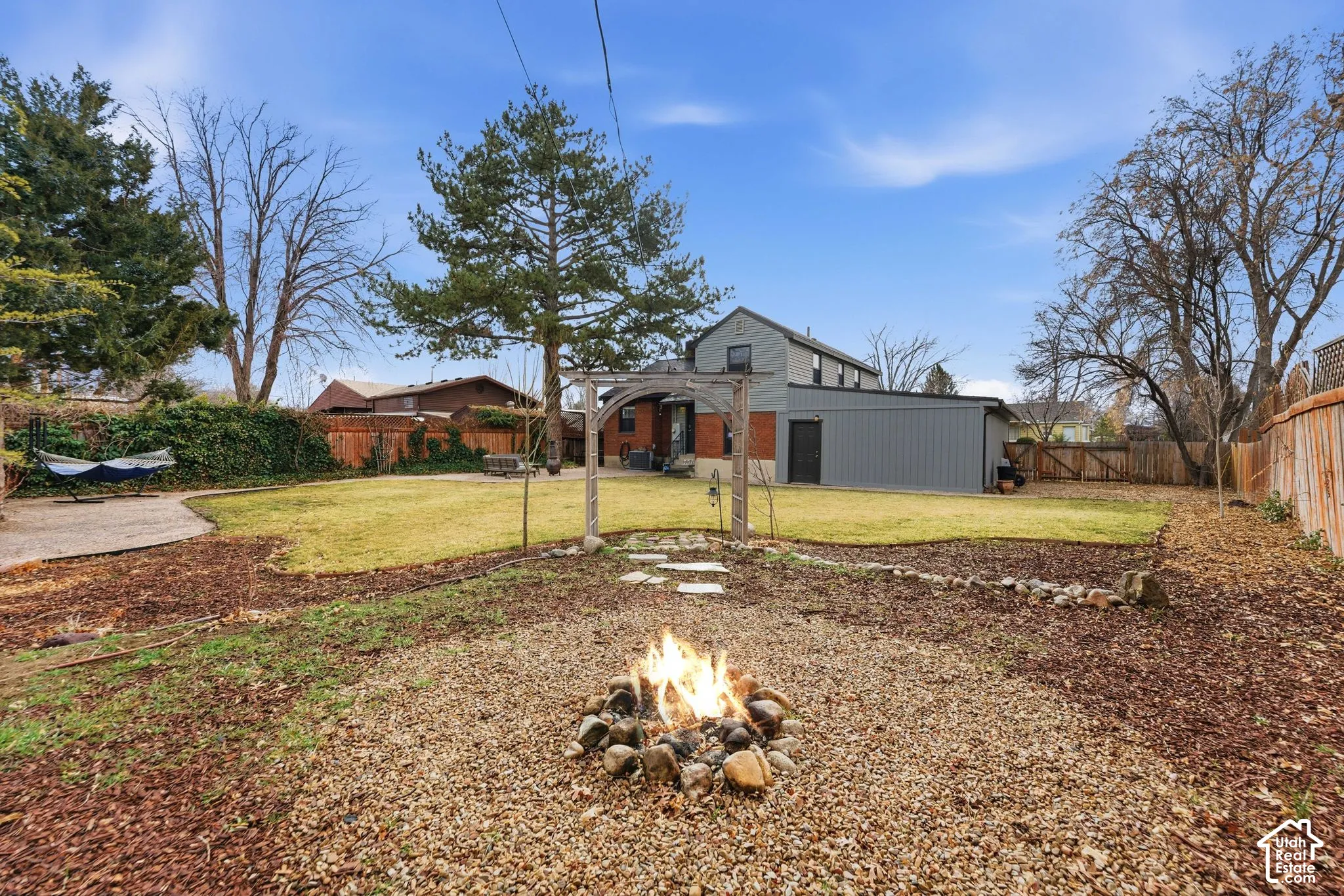 Expansive backyard featuring a manicured lawn, a gravel fire pit area, a concrete patio, a wood pergola, and a privacy fence