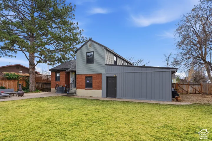 Expansive rear yard with a green lawn, brick and siding exterior, and a built-in storage structure