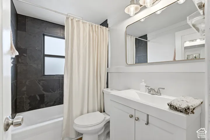 Tiled shower surround, frosted window, white bathtub, white vanity with integrated sink, and wall-mounted vanity lighting