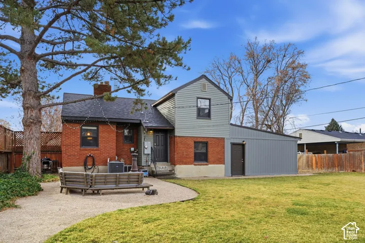 Expansive backyard featuring a gravel patio area, green lawn, mature tree, brick exterior, and a detached structure with a pitched roof