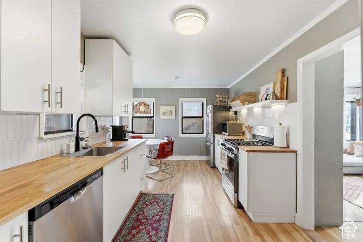 Modern kitchen with wood-finish flooring, white cabinetry, wood-finish countertops, stainless steel appliances, and a white tile backsplash