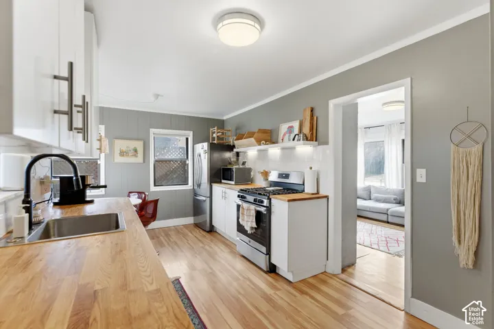 Kitchen featuring wood-finish flooring, white cabinetry with modern hardware, stainless steel appliances, and butcher block countertops