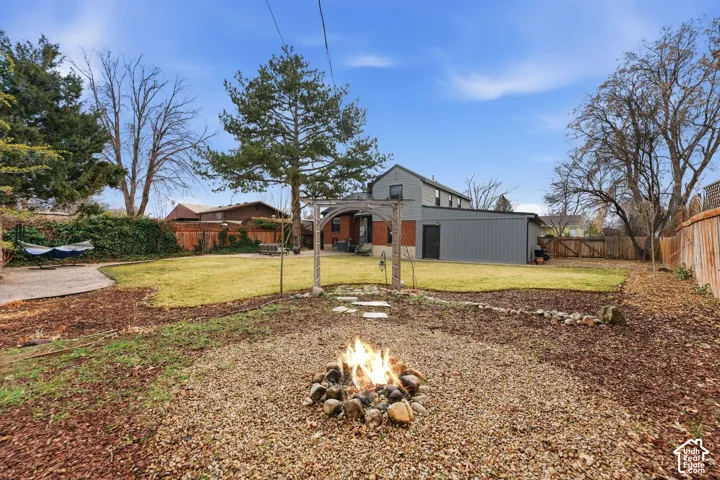 Expansive backyard featuring a manicured lawn, a gravel fire pit area, a concrete patio, a wood pergola, and a privacy fence