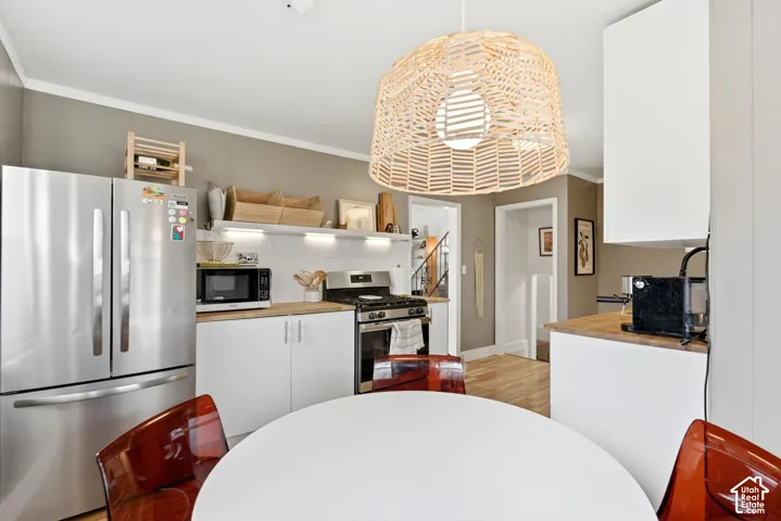 Stainless steel appliances, white cabinetry with silver hardware, light wood-finish countertops, white subway tile backsplash, and a woven pendant light fixture
