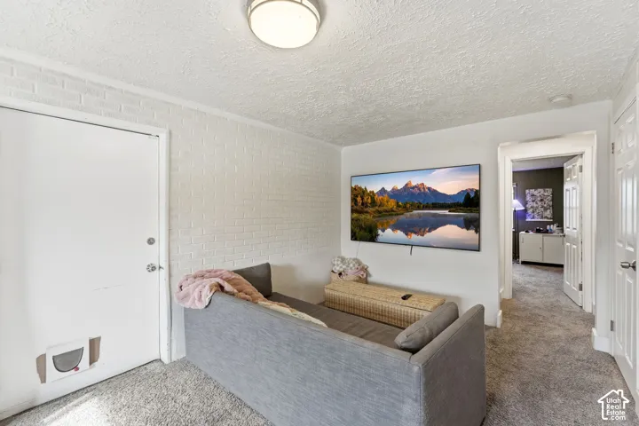 Carpeted flooring, white painted brick accent wall, white interior door, recessed ceiling light fixture, wall-mounted television