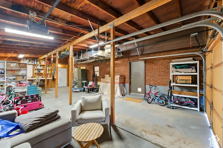 Garage space featuring exposed beam ceiling, concrete flooring, and brick wall accents