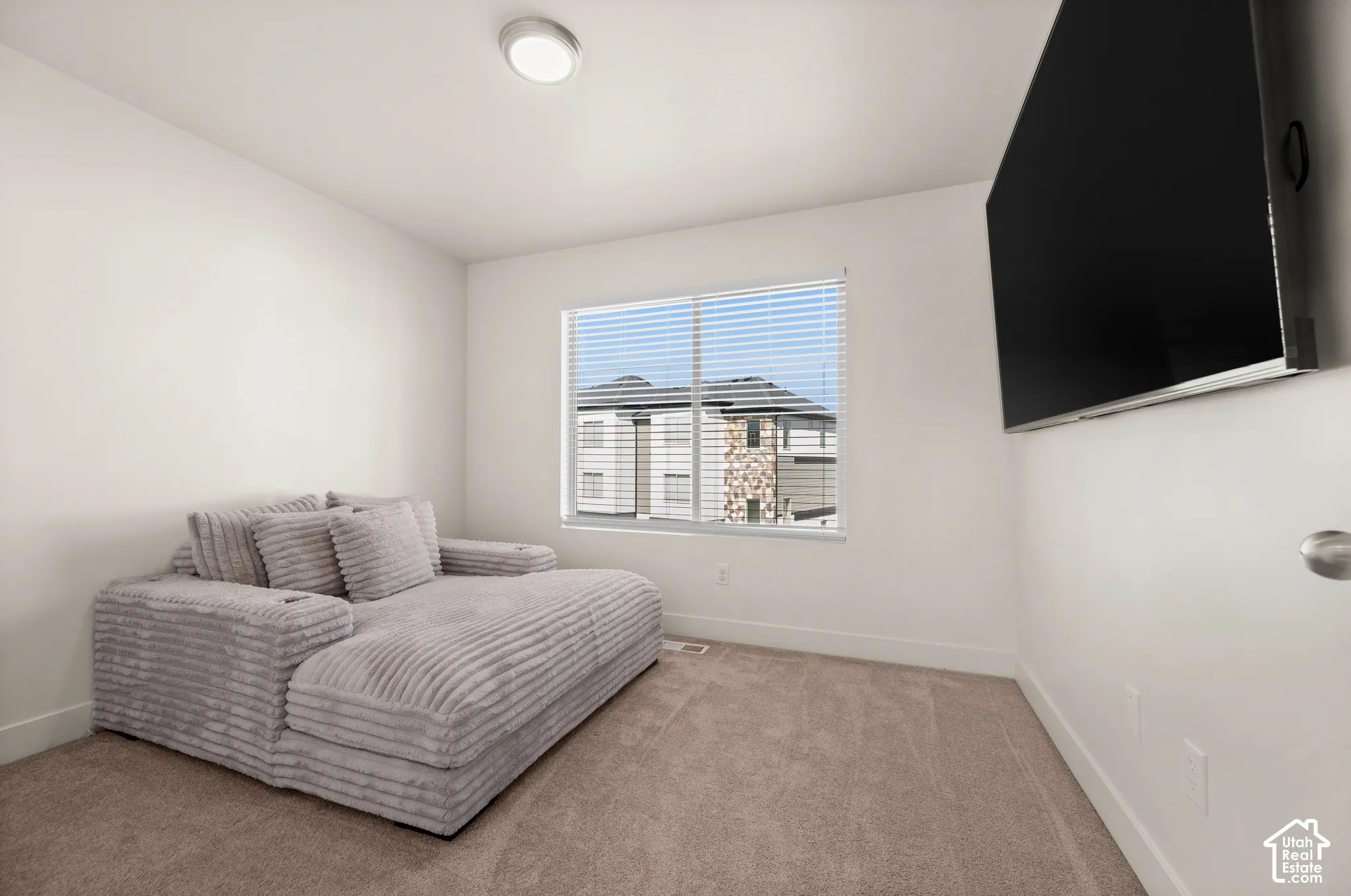 Recessed lighting, wall-mounted television, neutral carpet flooring, white window blinds, and a large window with exterior visibility