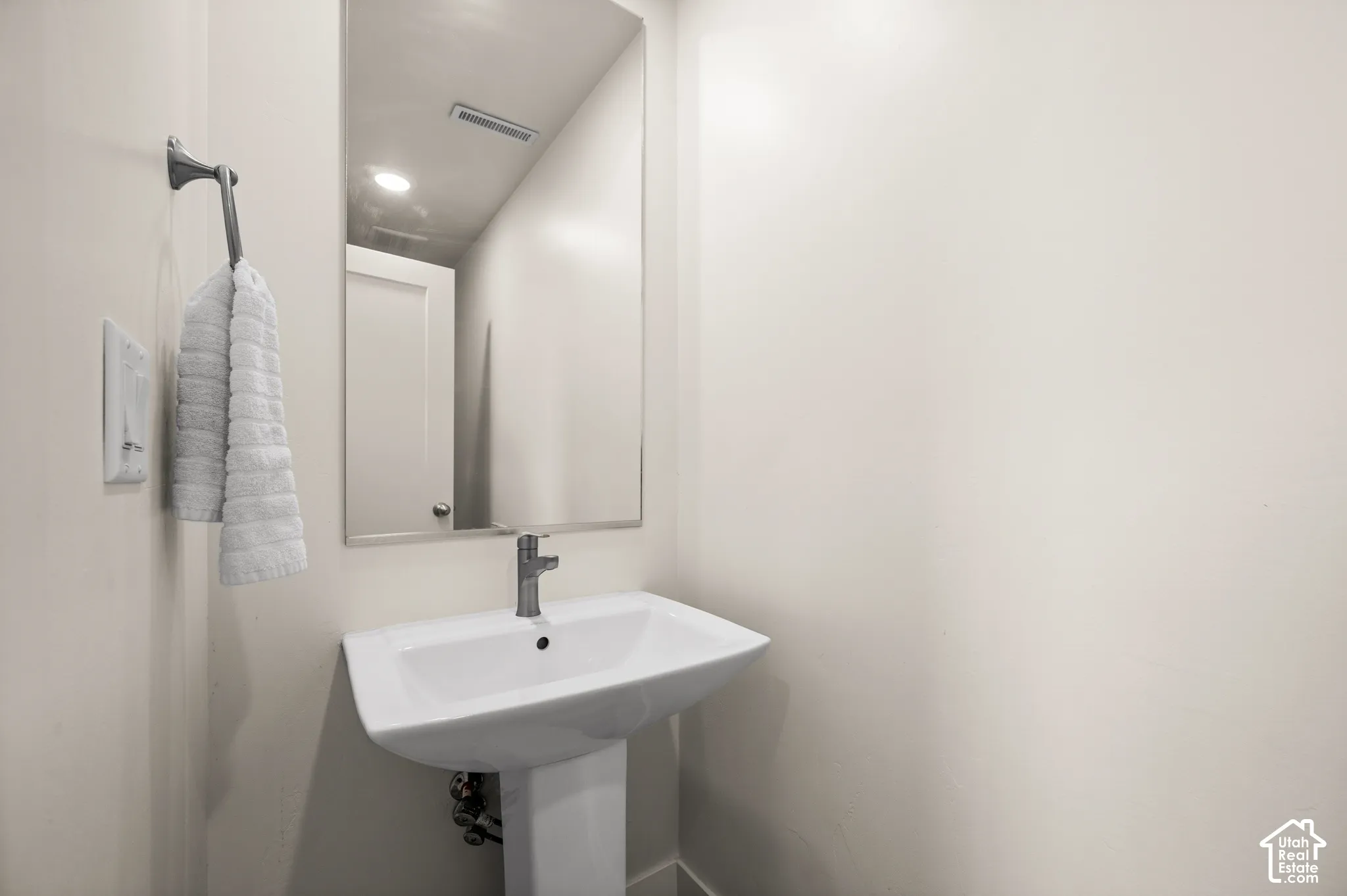 Pedestal sink with a polished chrome faucet, rectangular wall-mounted mirror, and neutral wall paint