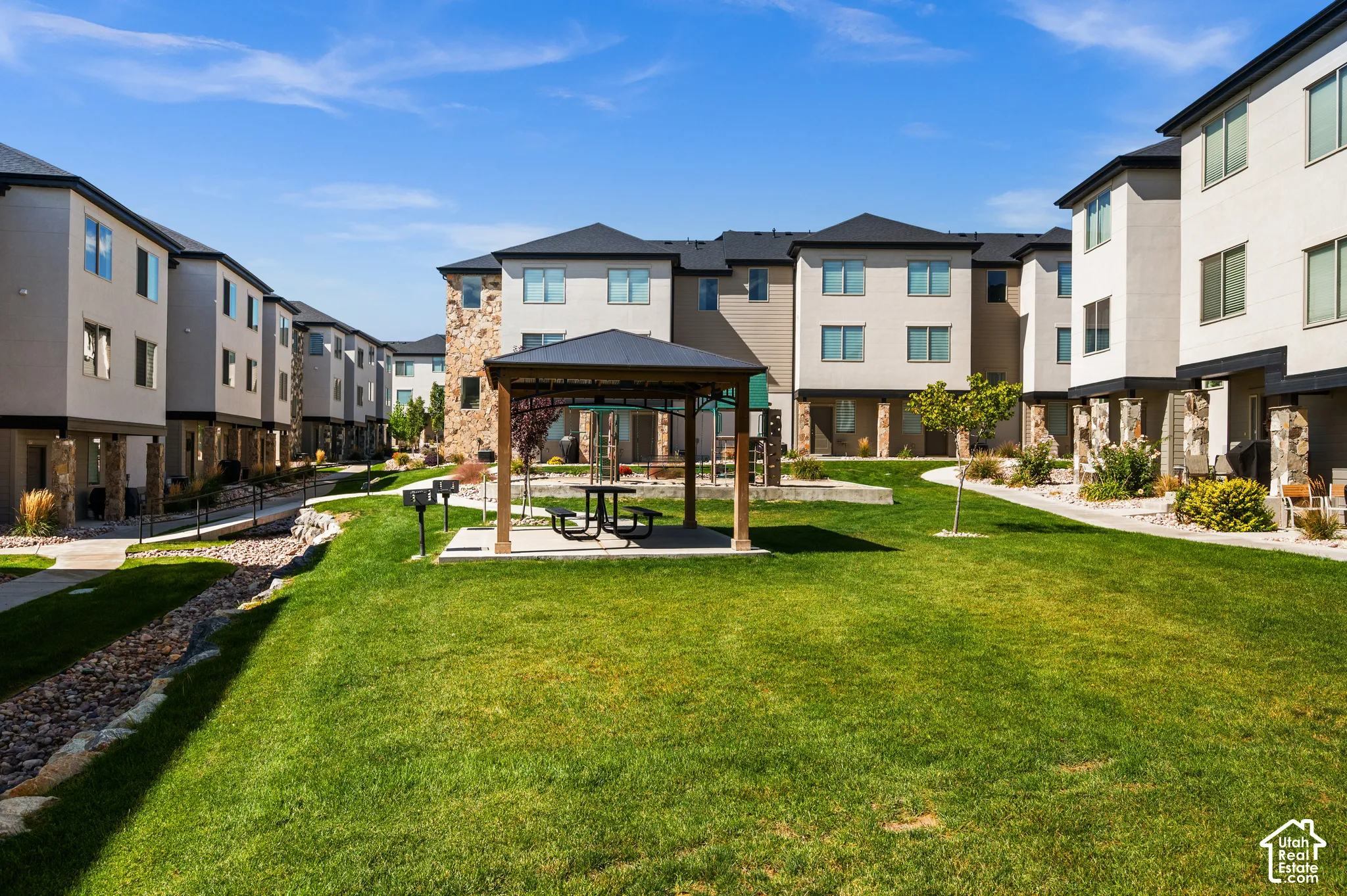 Manicured central green space with a covered gazebo and integrated BBQ grills, surrounded by multi-story residential buildings featuring stone and stucco exteriors