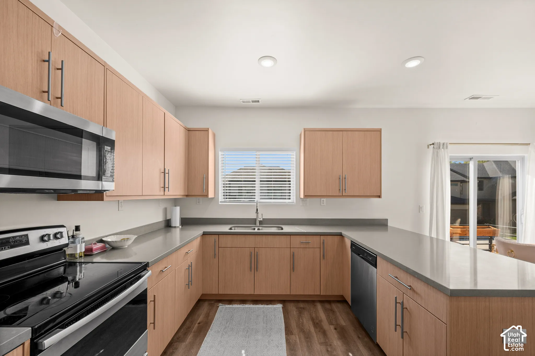 U-shaped kitchen with light wood-finish cabinetry, stainless steel appliances, grey countertops, and wood-finish flooring