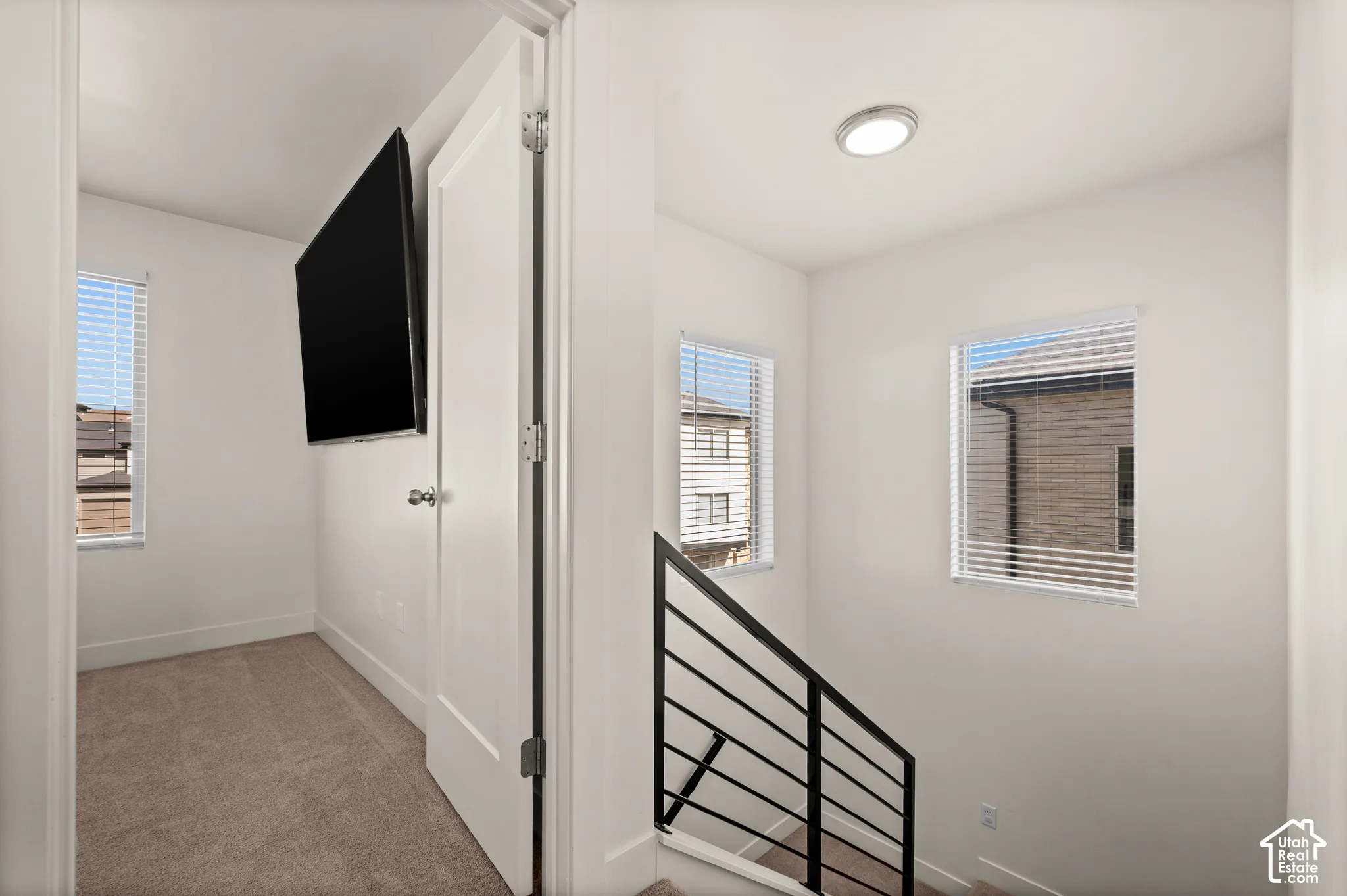 Carpeted room with a single window, a white door with a round knob, and a wall-mounted television
