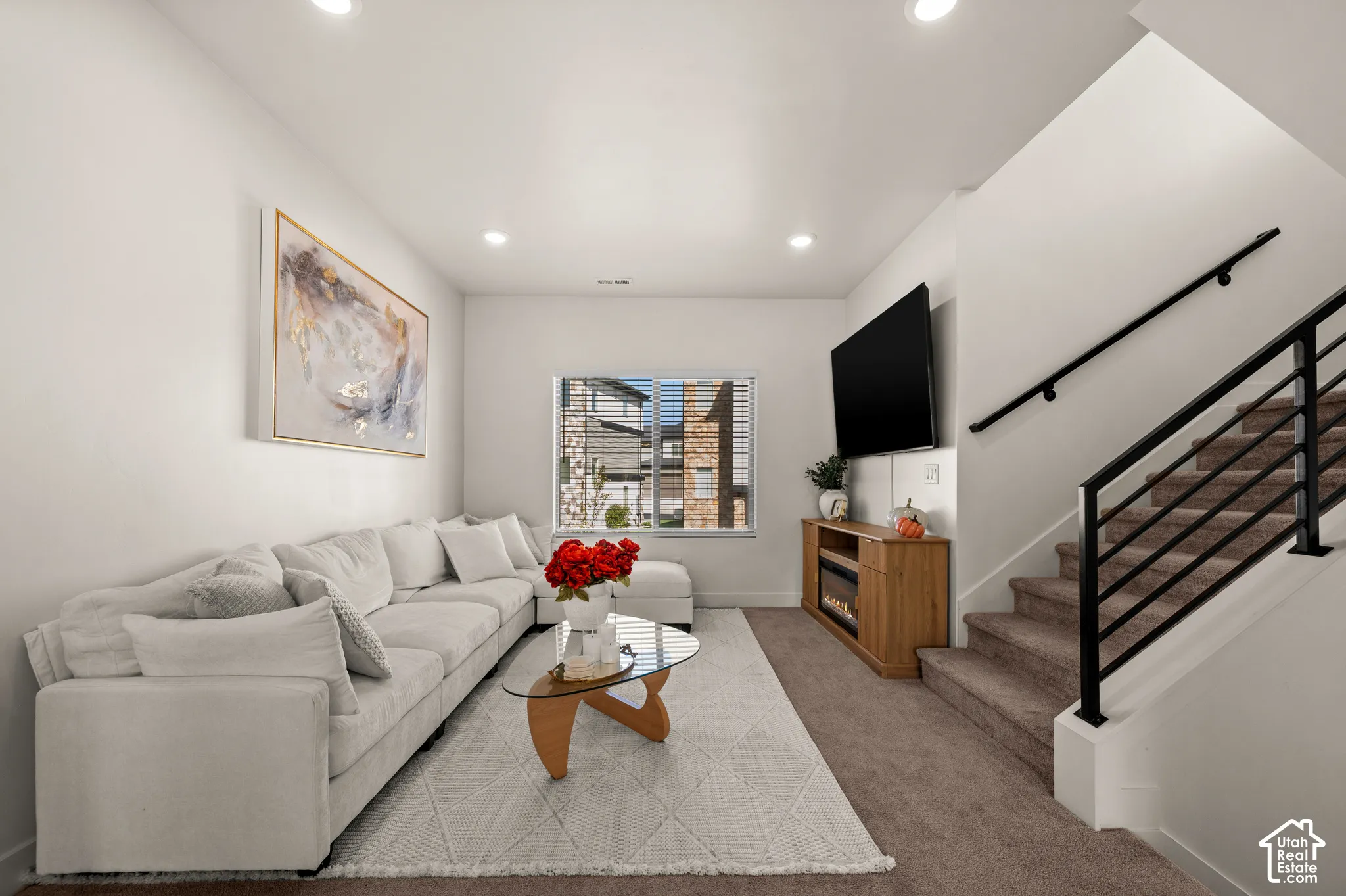 Recessed ceiling lighting, large window with blinds, built-in entertainment console with electric fireplace, and staircase with black metal railing