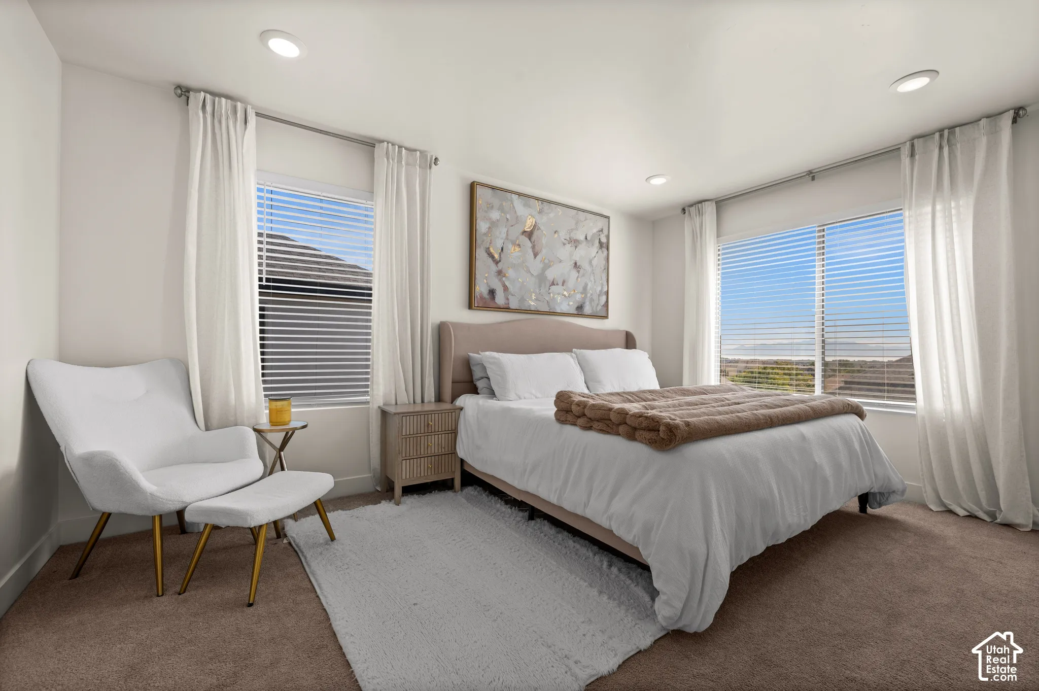 Recessed ceiling lighting, pair of large windows with blinds, light-colored walls, and neutral carpet