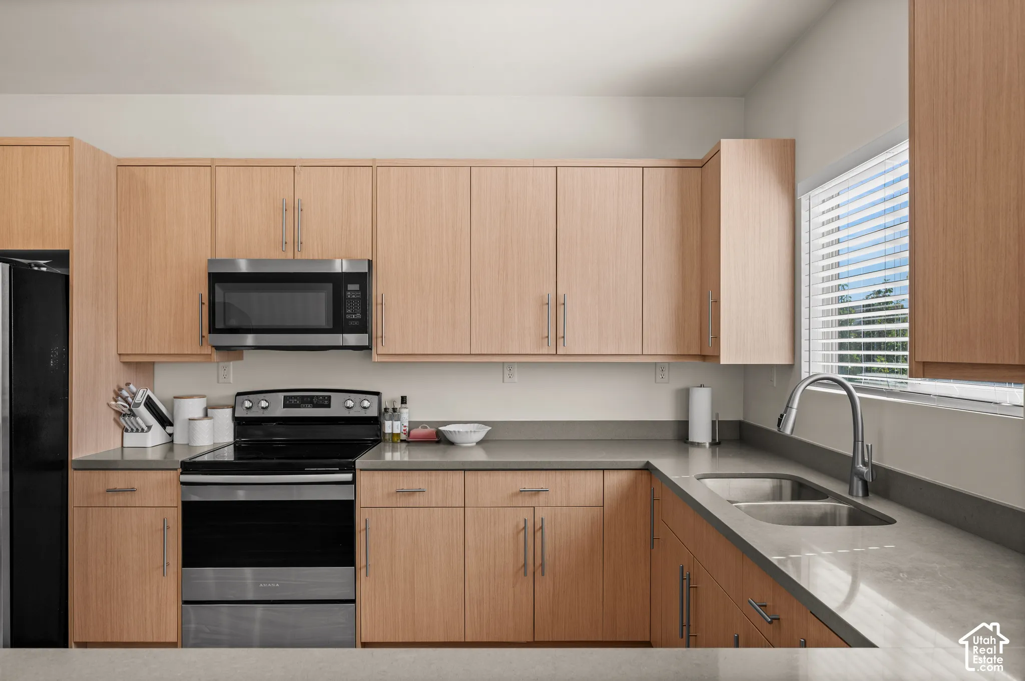 Full kitchen with light wood-finish cabinetry, stainless steel appliances, and grey countertops