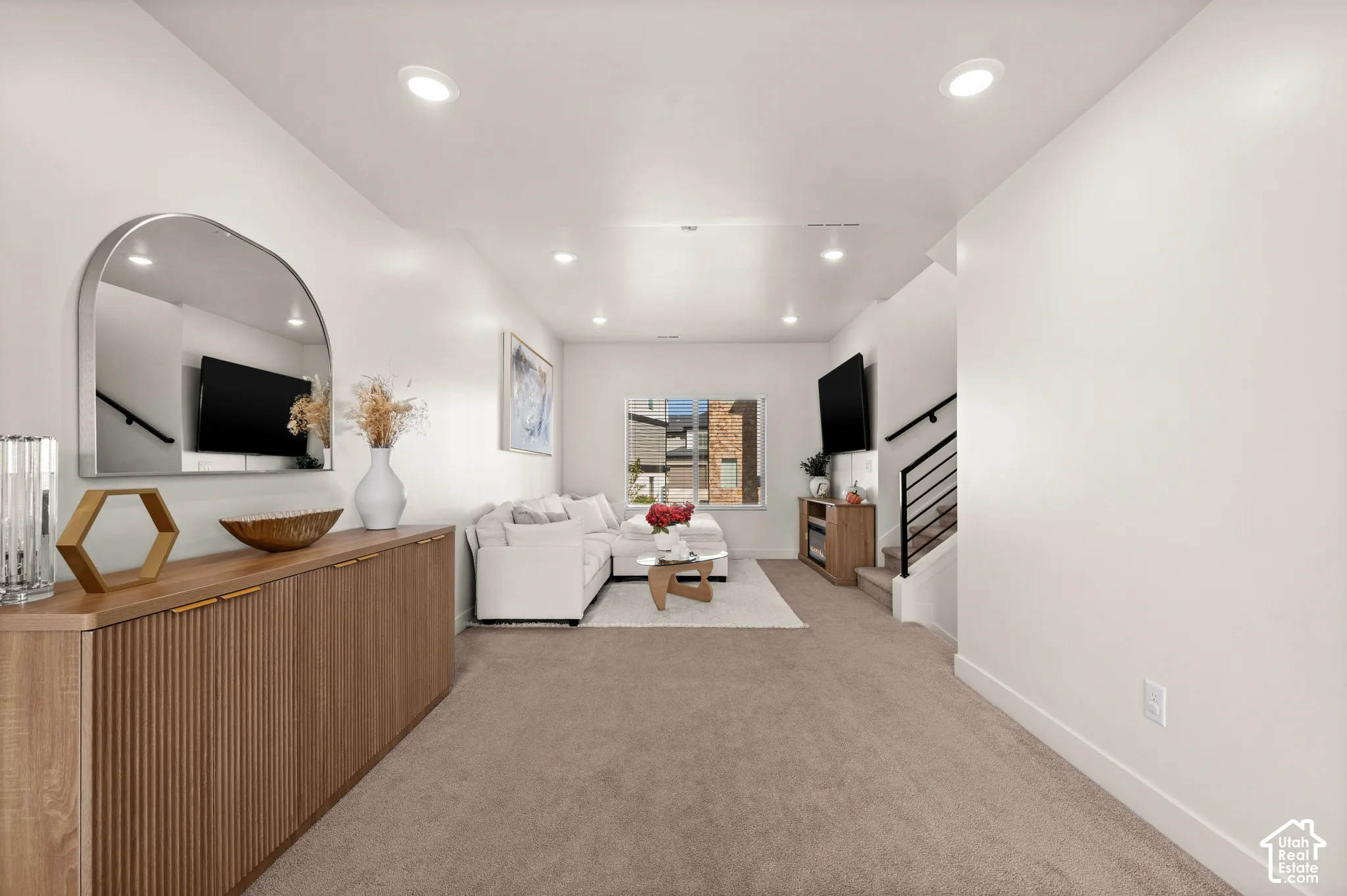 Recessed lighting, wood-finish console cabinetry, staircase with black metal railings, neutral wall paint, and natural light from exterior windows