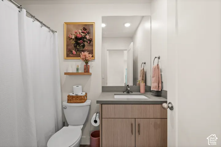 Vanity with a single basin sink and a gray countertop, wood-finish cabinetry, built-in mirror, and recessed lighting