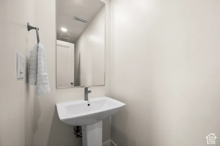 Pedestal sink with a polished chrome faucet, rectangular wall-mounted mirror, and neutral wall paint