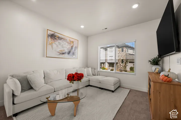 Recessed ceiling lighting, large window with blinds, wood-finish console table, and wall-mounted television