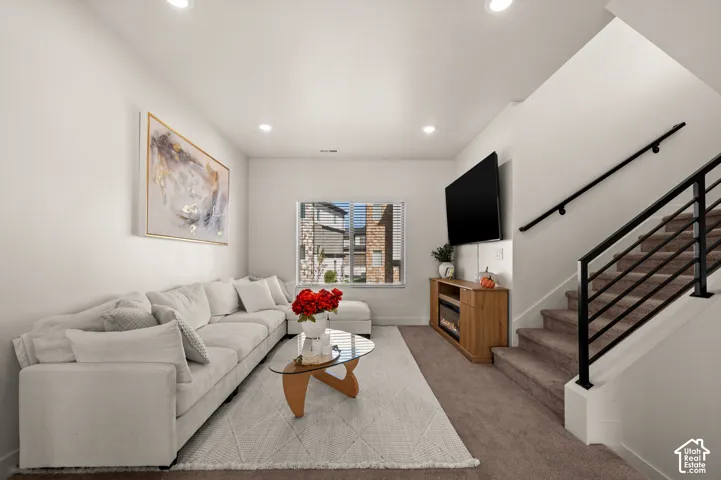 Recessed ceiling lighting, large window with blinds, built-in entertainment console with electric fireplace, and staircase with black metal railing