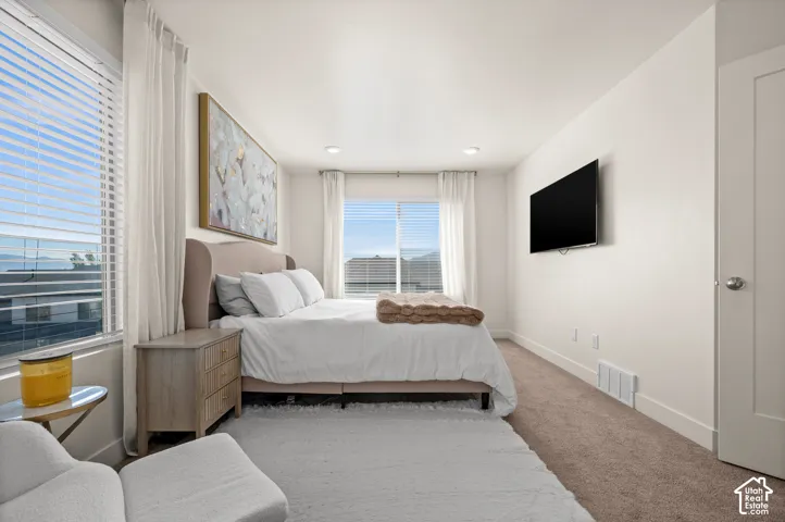 Recessed lighting, large windows with blinds, wall-mounted television, and neutral carpeting