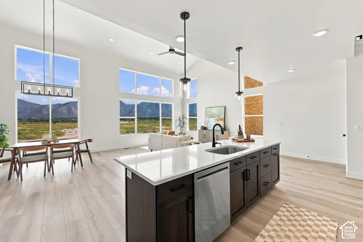 Open-concept living area with vaulted ceilings, expansive windows, light wood-finish flooring, a kitchen island with a stainless steel sink, and a black hardware kitchen