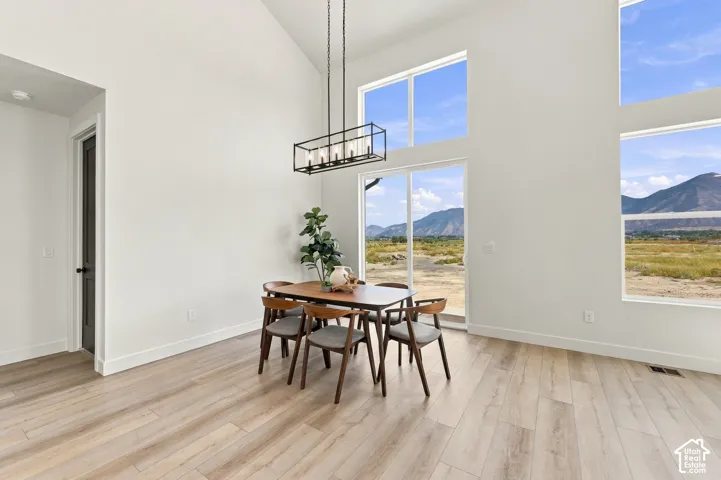 Vaulted ceiling, wood-finish flooring, multiple large windows, sliding glass door, and a modern rectangular chandelier