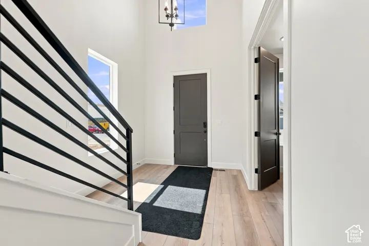 Entryway with wood-finish flooring, a two-story ceiling, a contemporary chandelier, and a black metal staircase railing