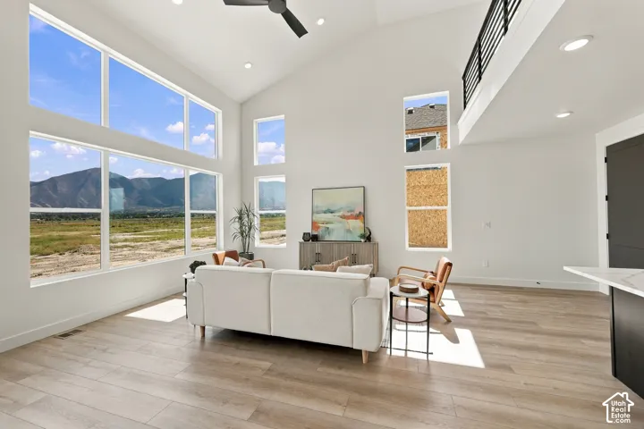 Vaulted ceiling with a ceiling fan, abundant natural light from large windows, mountain and field scenery, wood-finish flooring, and a metal railing on the upper level