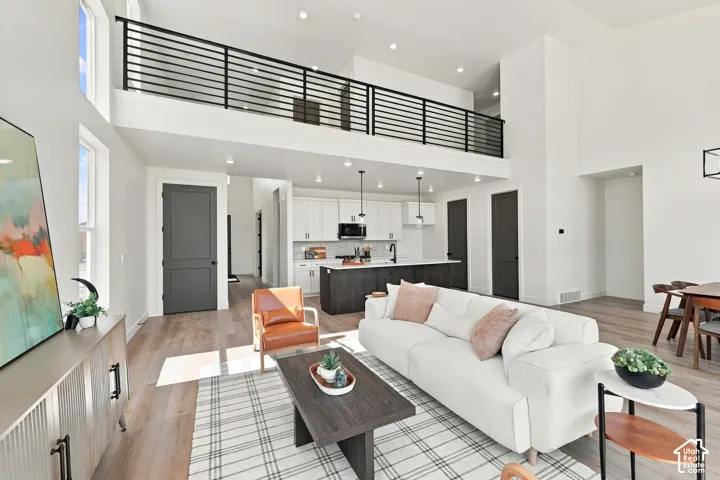 Two-story living area with high ceilings, wood-finish flooring, and an open-concept kitchen featuring an island with pendant lighting