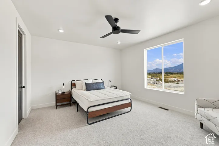 Bright bedroom with light-colored carpeting, a large window, recessed lighting, and a ceiling fan