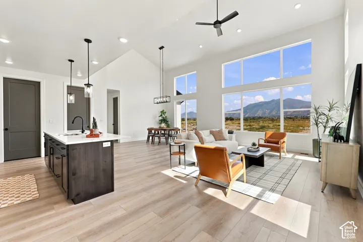 Vaulted ceiling with a black ceiling fan, wood-finish flooring, a kitchen island with a white countertop, large windows, and recessed lighting