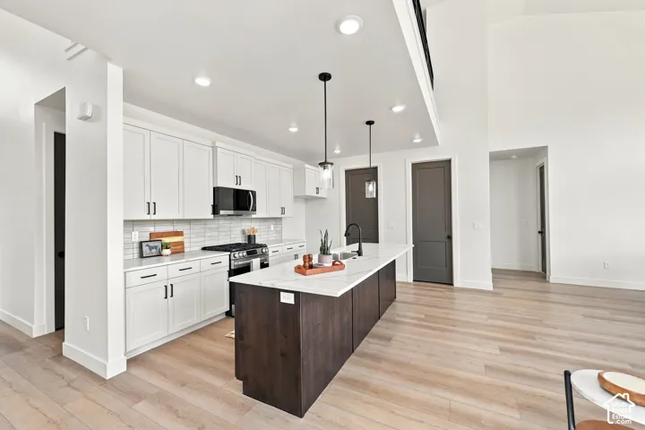 Modern kitchen featuring white shaker cabinetry, stainless steel appliances, a center island with pendant lighting, and wood-finish flooring