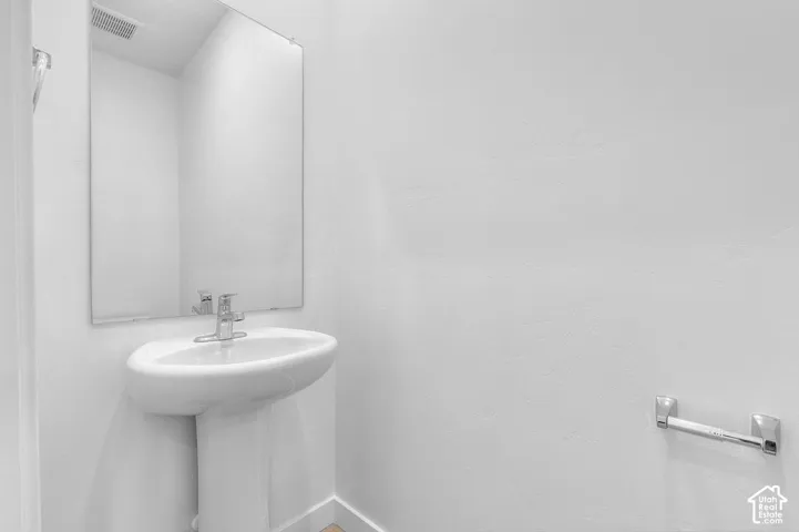 Pedestal sink with chrome faucet, wall-mounted mirror, and chrome towel bar