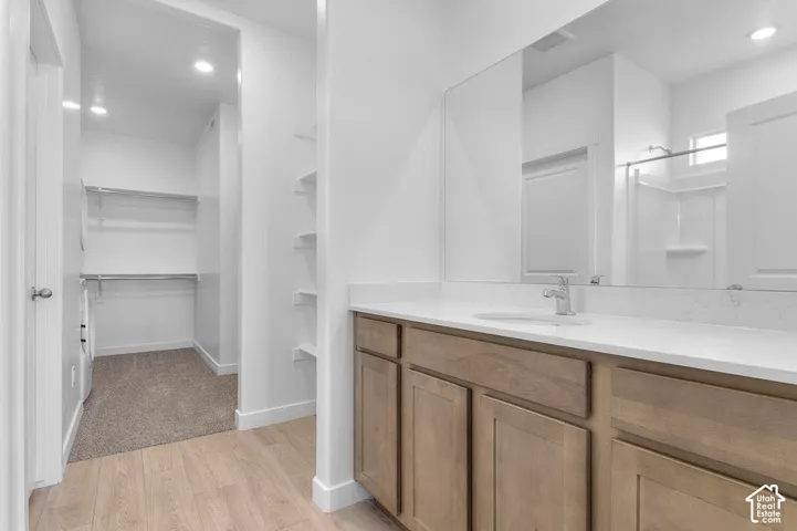 Wood-finish flooring, light wood cabinetry, white countertop, integrated sink, and a large wall-mounted mirror