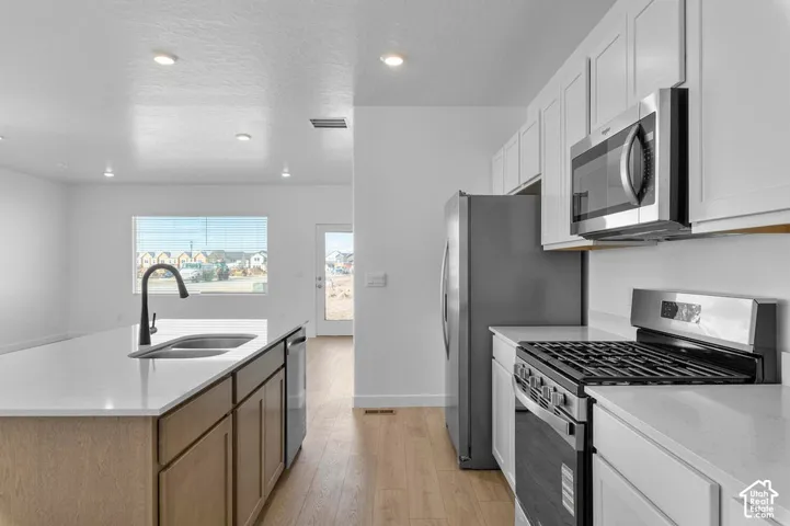 Kitchen featuring white shaker cabinetry, stainless steel appliances, a center island with a sink, light wood-finish flooring, and recessed lighting
