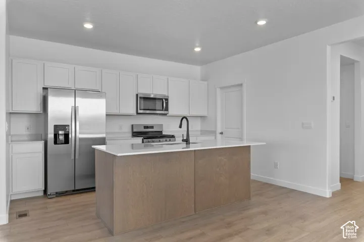 Modern kitchen featuring light wood-finish flooring, white cabinetry, a wood-finish island with a light-toned countertop, and stainless steel appliances