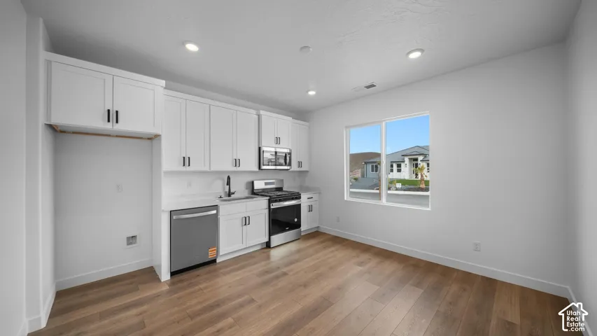 Contemporary kitchen featuring white cabinetry, stainless steel appliances, a white solid surface countertop, wood-finish flooring, and recessed lighting