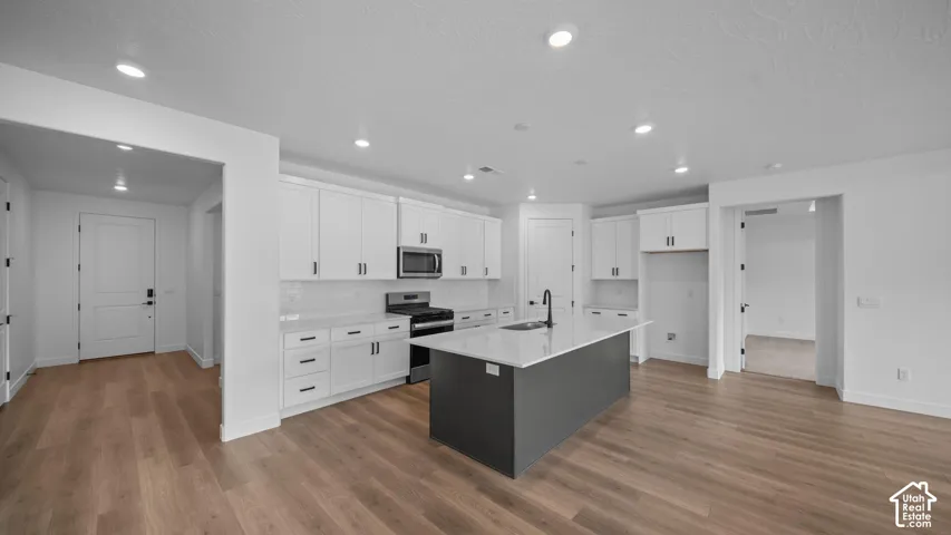 Open-concept kitchen featuring white cabinetry, stainless steel appliances, a dark-toned island with a light countertop, and recessed lighting