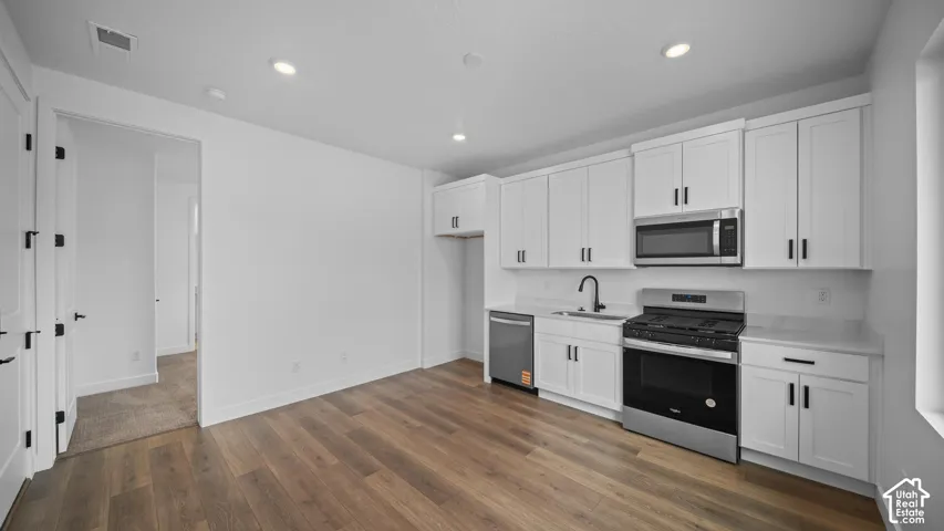 Kitchenette featuring white shaker-style cabinetry, wood-finish flooring, stainless steel appliances, a black faucet, and recessed lighting