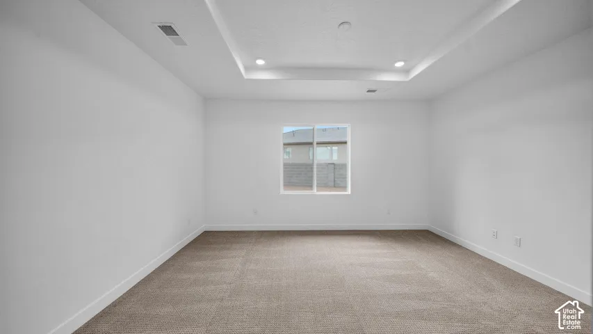 Spacious room featuring neutral carpeting, a tray ceiling with recessed lighting, and a window with white trim